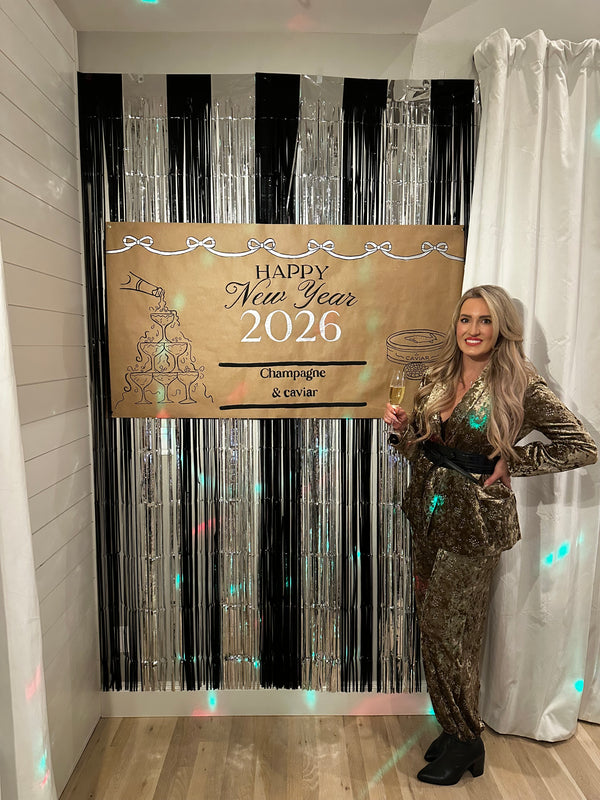 A black and silver tinsel wall hanging behind a custom hand-lettered banner for a new years eve party with a champagne and caviar theme.
