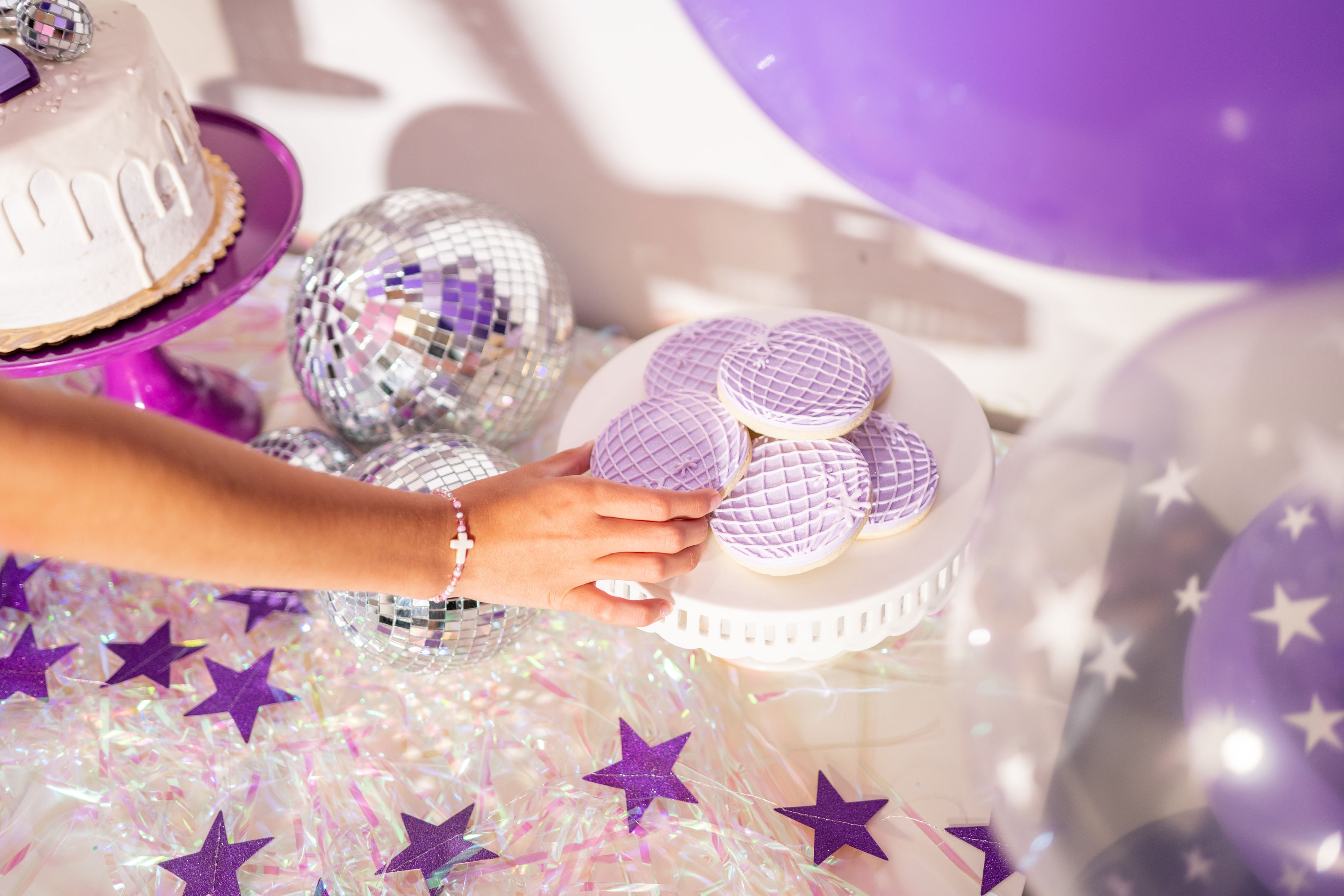 Snack table ideas for a sweet sixteen birthday party or purple party theme for teens with disco ball cookies and a purple glitter star garland.