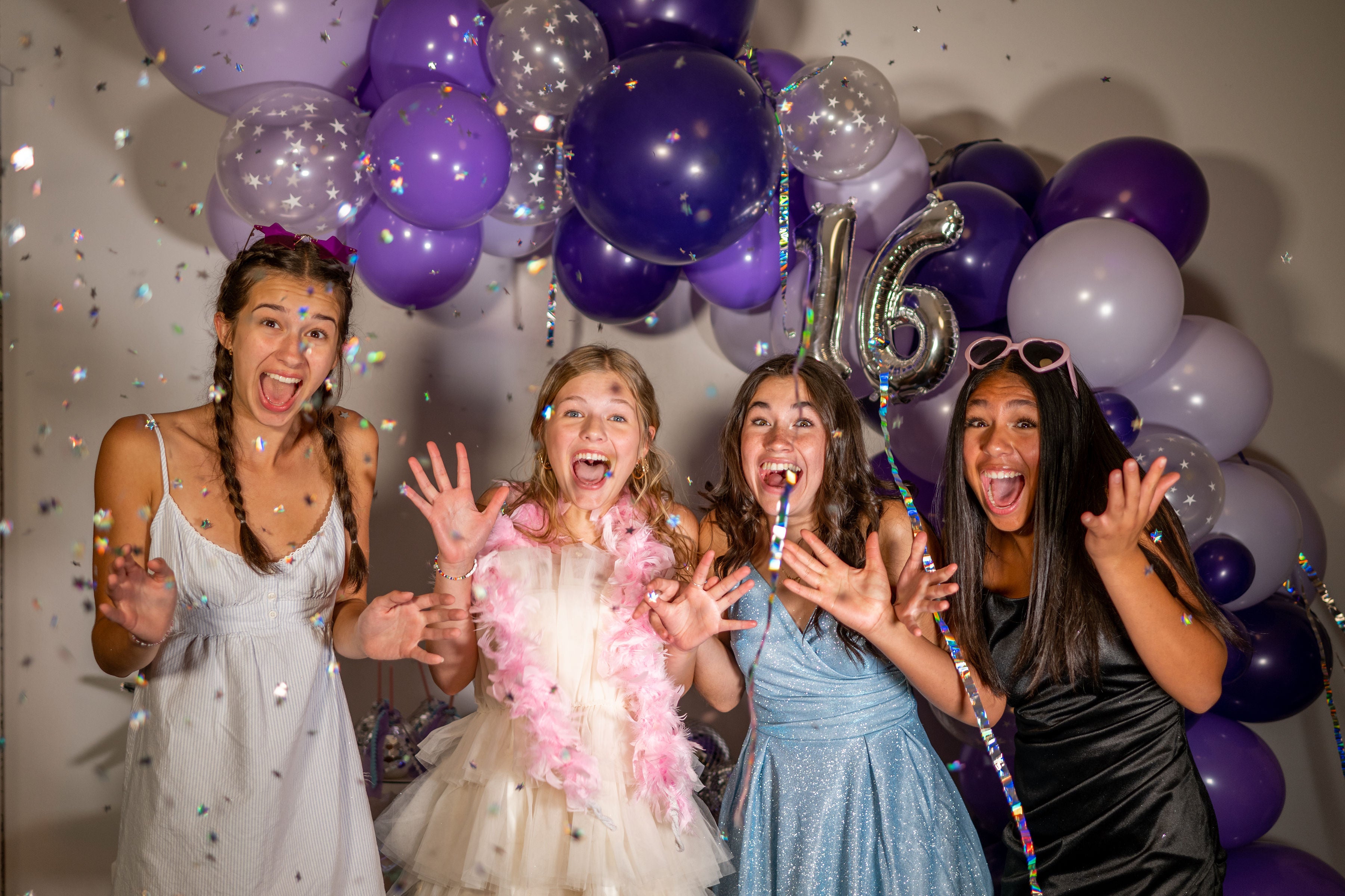 Four girls in front of a purple sweet sixteen photo shoot backdrop with a DIY purple balloon garland.