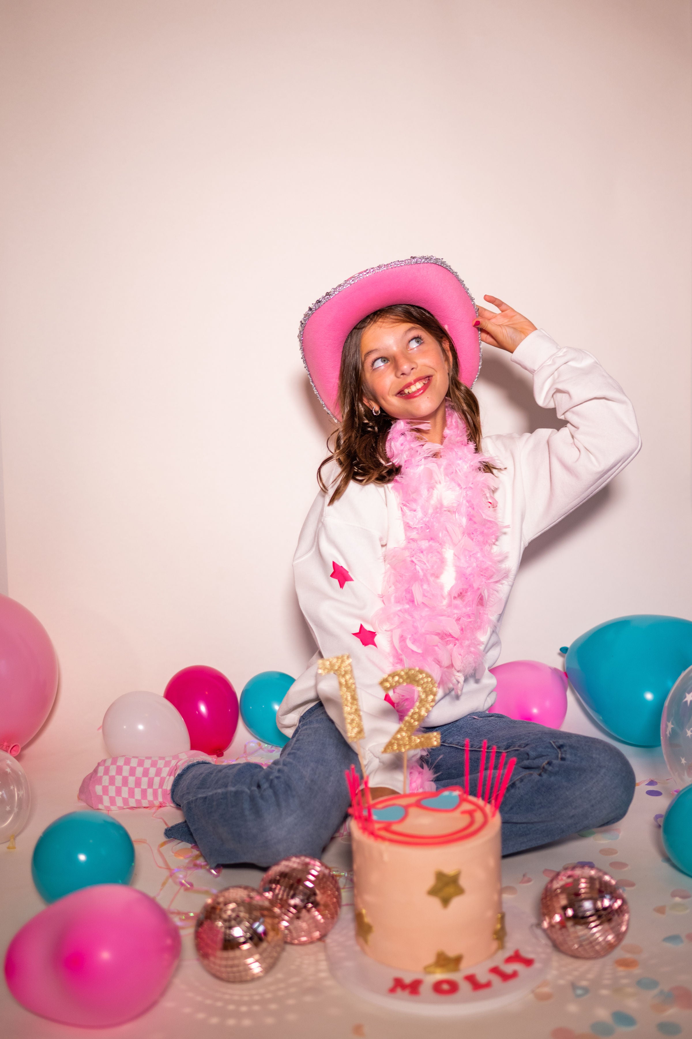 Photoshoot inspiration for a Barbie birthday party for teens or tweens with DIY pink and aqua balloon garland decor, pink disco ball decorations, and a pink cowgirl hat.