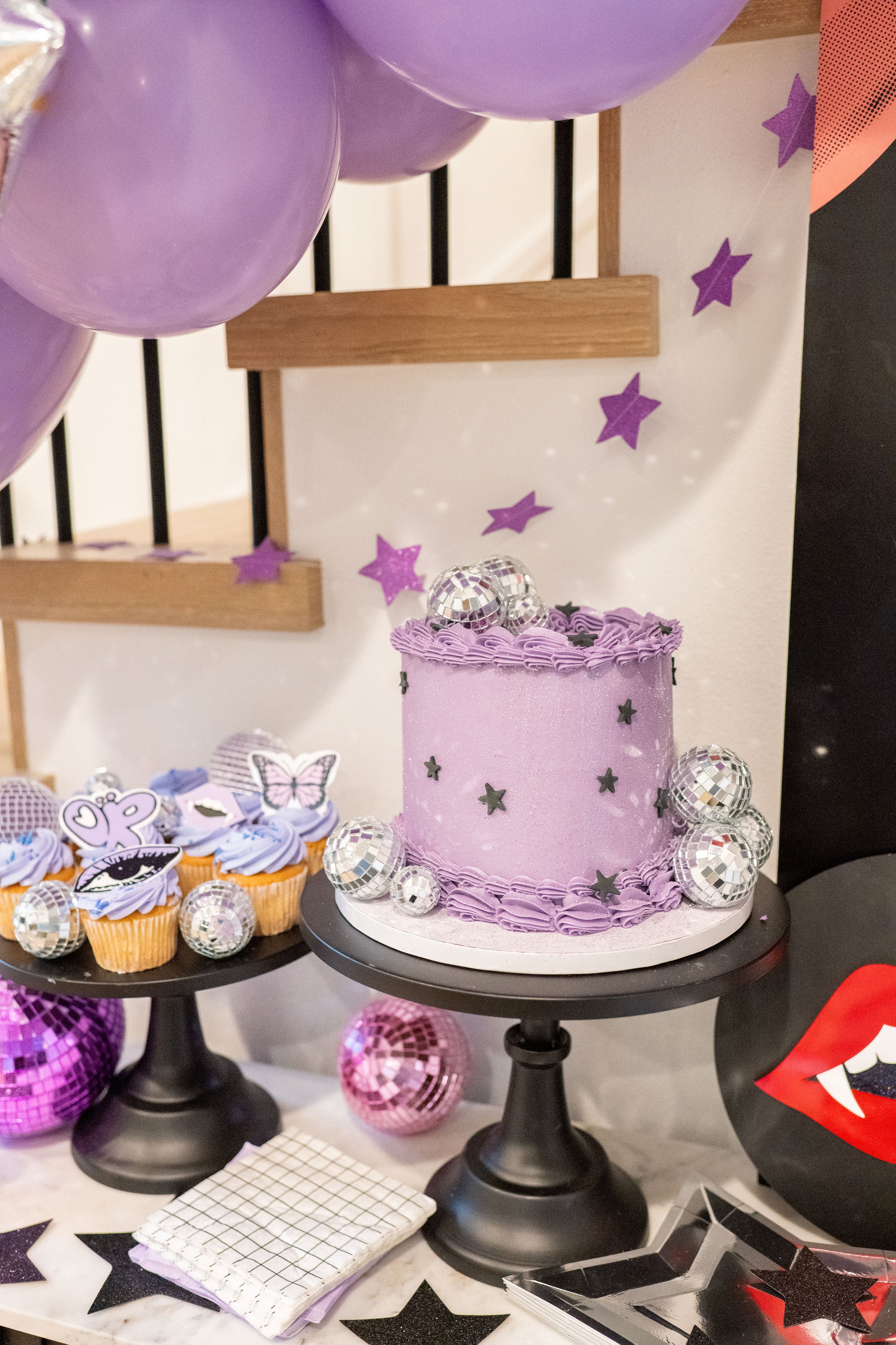 A tween party inspiration detail shot featuring an Olivia Rodrigo birthday cake and purple cupcakes set next to purple disco balls, silver star paper plates, and a purple star garland.