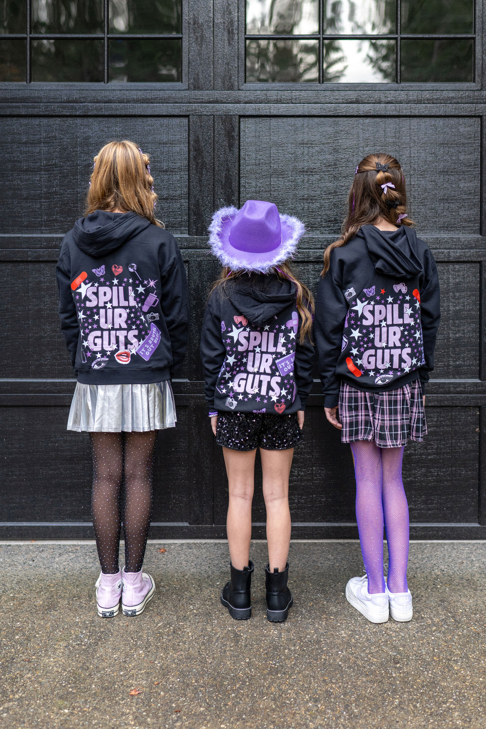 Three girls wearing custom spill ur guts hoodie party favors at an Olivia Rodrigo-themed birthday party for tweens or kids.