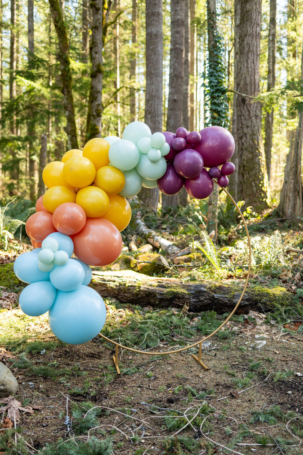 A muted multicolor balloon garland kit mounted on a gold decorative arch as a photo backdrop or party decoration for a Taylor Swift tea party or rustic glam garden party for tweens or teens, or a bridal shower theme idea for Swifties.