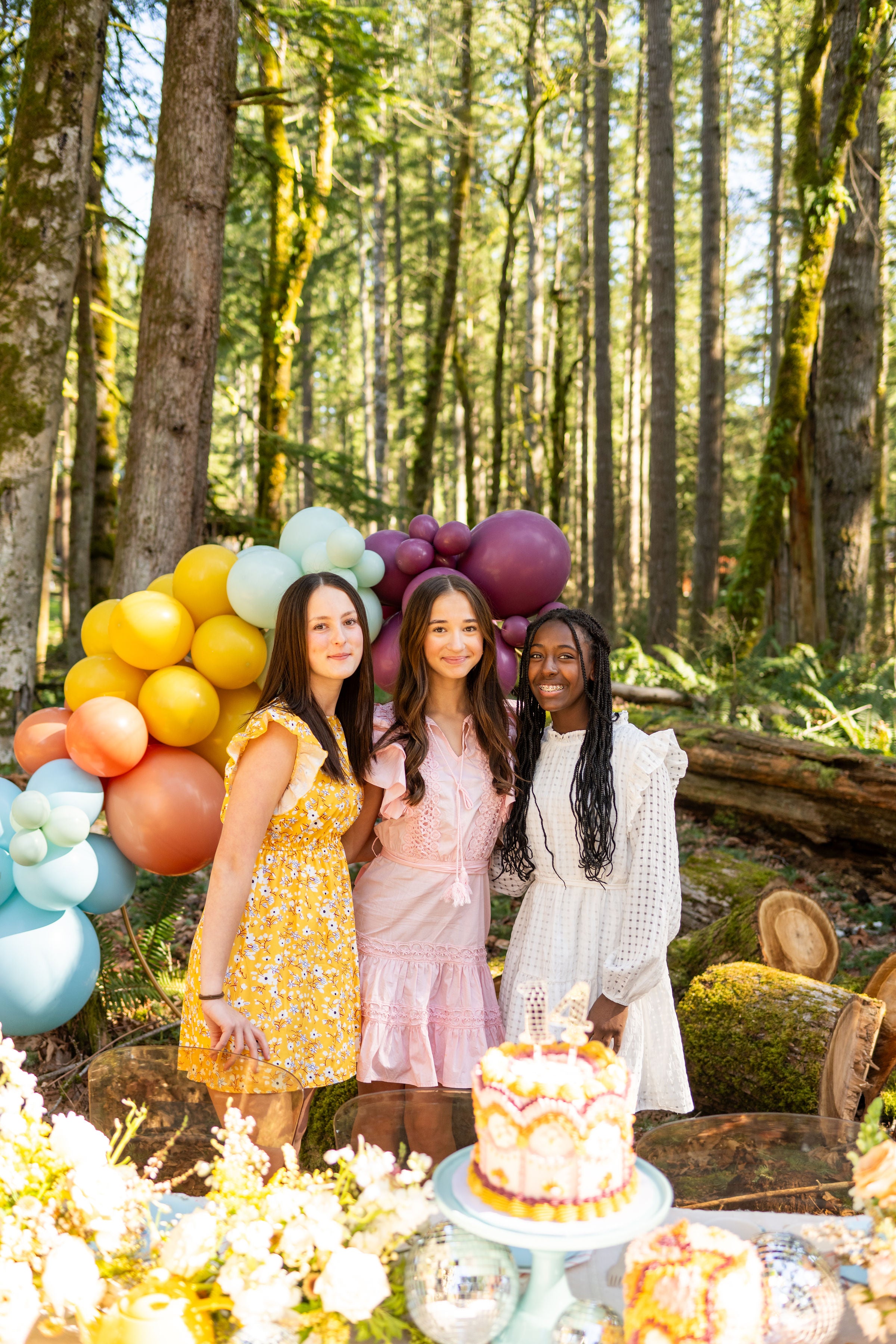 Photo shoot ideas for a Taylor Swift Anti Hero Midnights Birthday Party for teens, including a Taylor Swift cake table and a blue, peach, yellow, mint, and purple diy balloon garland kit fixed to a gold decorative arch.