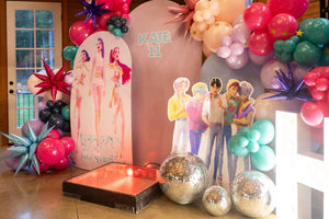 A photo shoot backdrop for a kpop demon hunters party for kids or tweens, featuring kpop demon hunters character cutouts and a diy balloon arch kit.