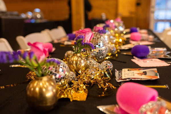 Party supplies and tableware for a kpop demon hunters party for weens or kids, featuring gold and silver disco ball table decorations and a gold tinsel garland.