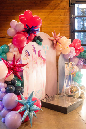 A photo shoot backdrop for a kpop demon hunters party for kids or tweens, featuring kpop demon hunters character cutouts and a diy balloon arch kit.