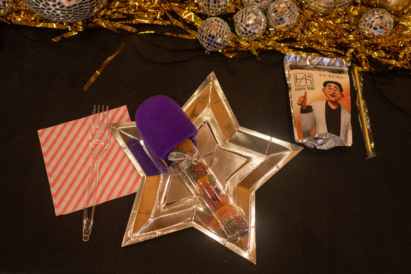 Tableware for a Kpop Demon Hunters party for tweens or kids, featuring gold star paper plates and a candy filled microphone.