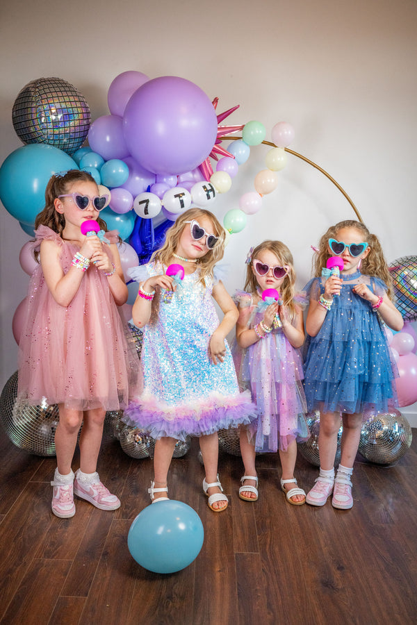 Four girls sing karaoke with microphone party favors at a Taylor Swift Eras Tour themed birthday party for kids, tweens, or teens, in front of a Taylor Swift diy balloon arch kit.