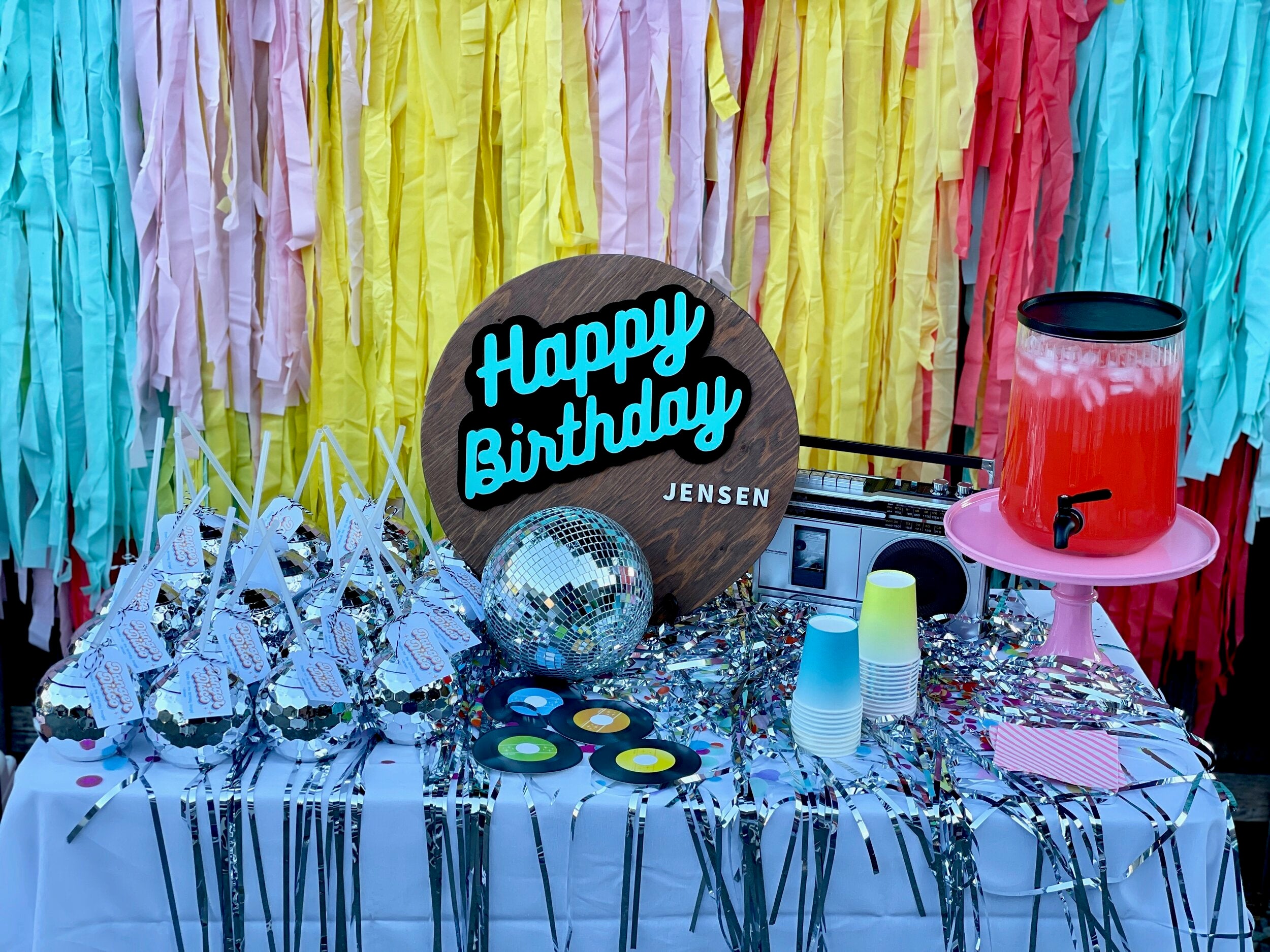 Party favor table idea for a disco party theme kit for adults, kids, or teens, with disco ball tumblers, yellow and blue paper cups, and yellow, blue, and lilac party streamers.