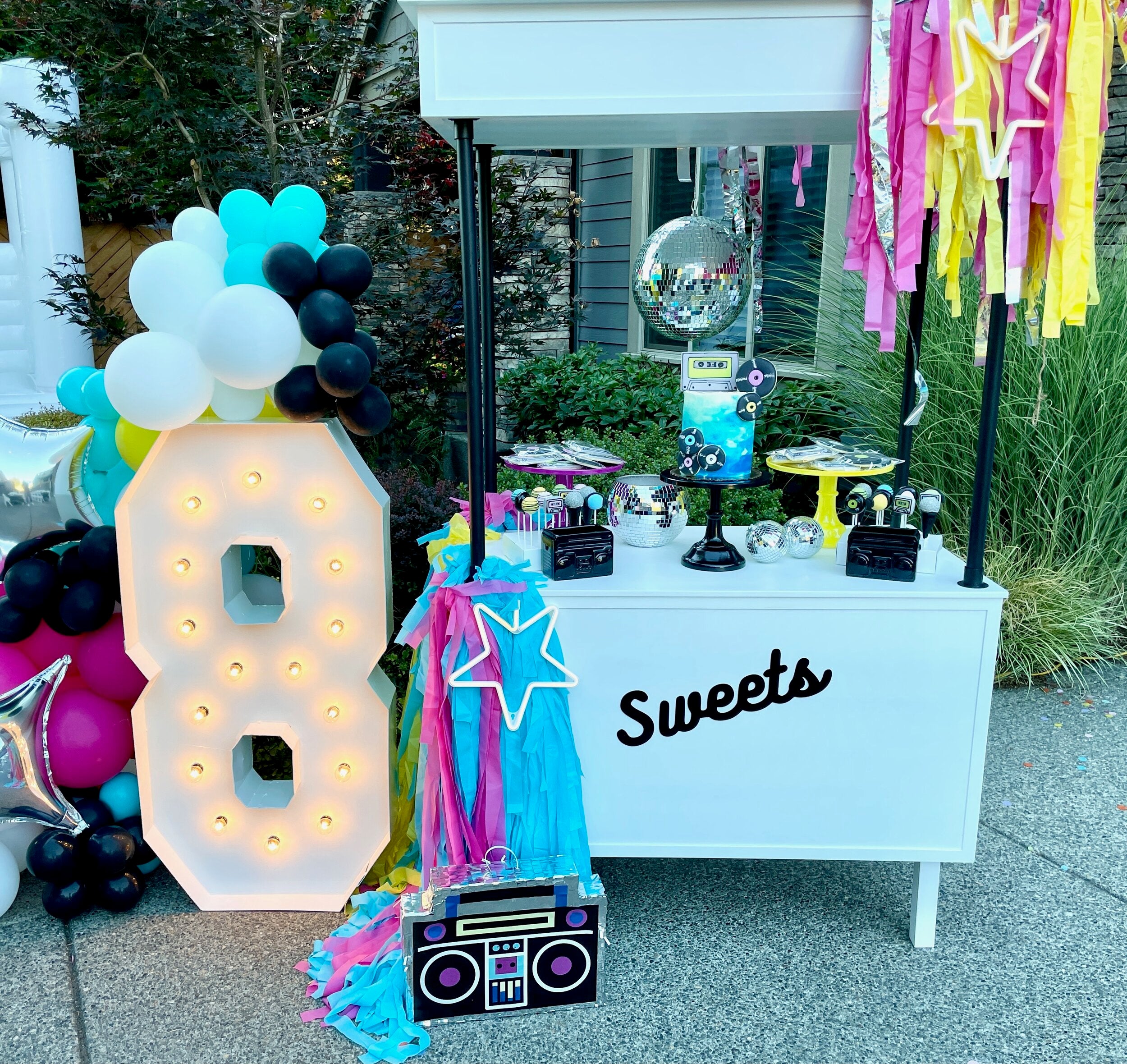 8-year old birthday inspiration with a disco party theme, including kids birthday party cake table decor ideas with marquee letter sign, inflatable foil disco ball, and balloon garland.