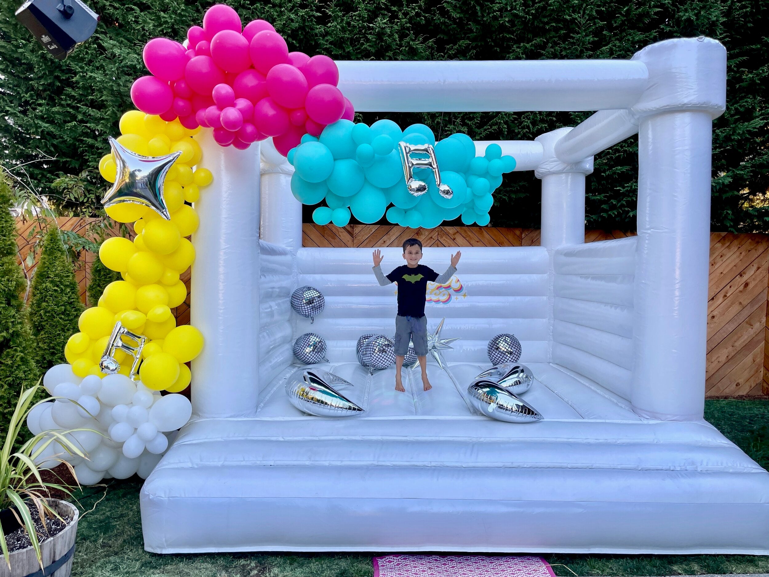 A yellow, pink, blue, and white balloon garland kit for a DIY 80s theme disco party for kids, with inflatable disco ball party decor.