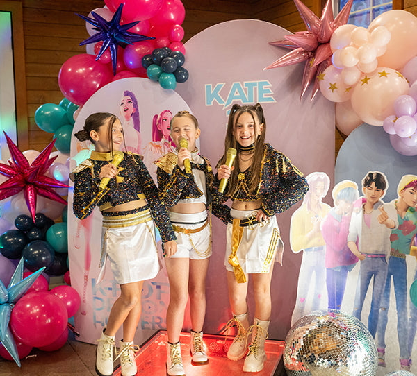 A photoshoot at a Kpop birthday party for tweens or kids, featuring Kpop Demon Hunters photo backdrop decorations including a hot pink balloon garland kit.