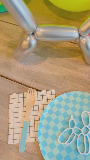 Party supplies for a tween or teen birthday party with balloon animal decorations and bright, fun colored paper plates and forks.